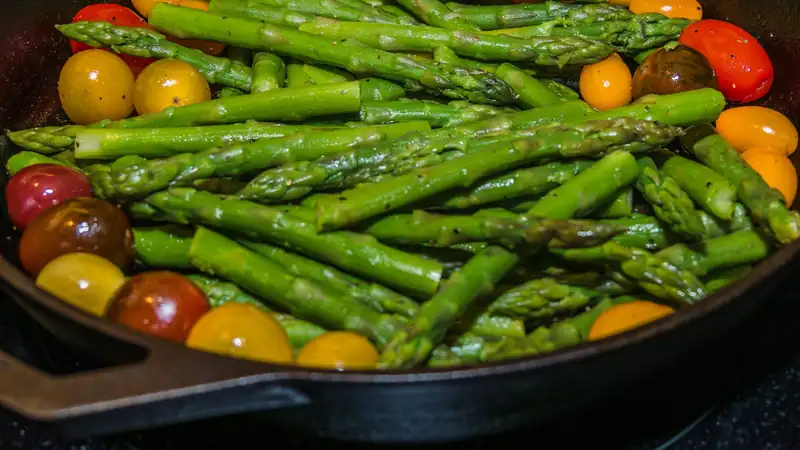 Asparagus and cherry tomatoes searing in a well-seasoned cast-iron skillet.