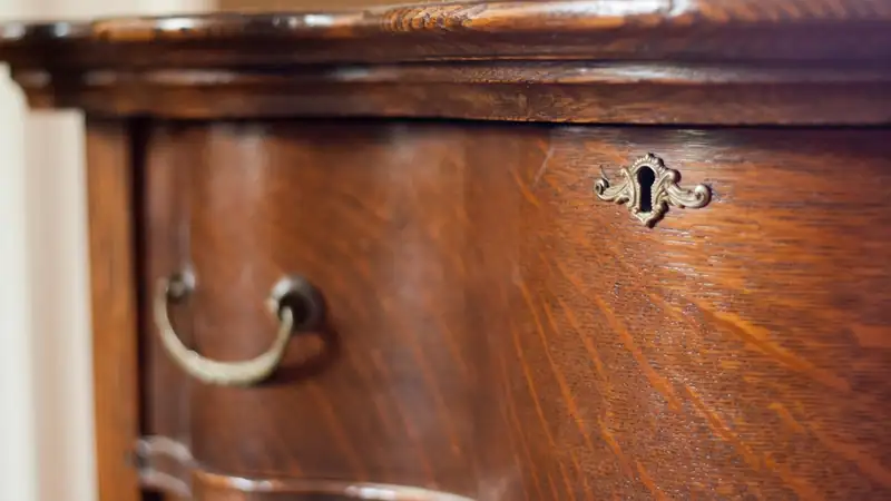 Close-up of a wooden dresser's curved drawer front with a brass bail pull and a keyhole plate.