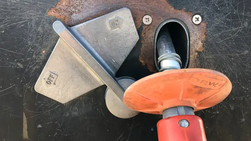 Close-up of a fuel nozzle resting in a worn, rust-edged pump holster beside its on-off lever.