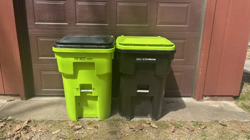 Two large wheeled trash bins, one lime green and one black, in front of a brown garage door.
