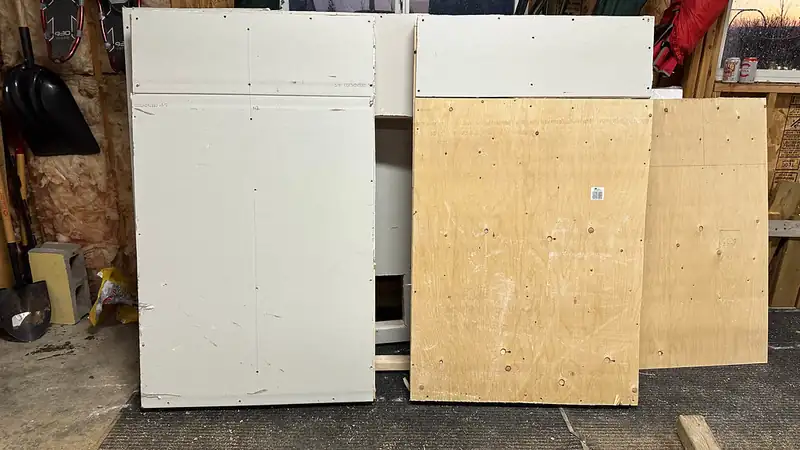 Sheets of drywall and plywood panels leaning against a wall in a garage workshop.