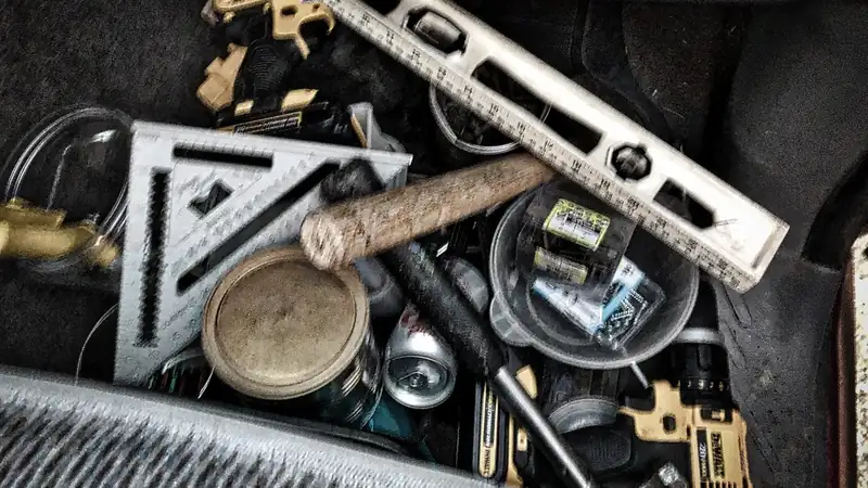 A work bucket packed with a level, speed square, hammer, tape and drill parts.