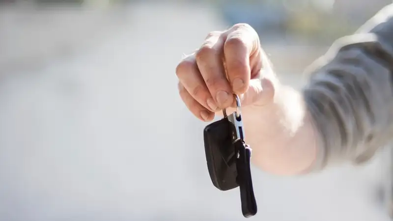 A hand holding out a car key fob against a soft, blurred background.