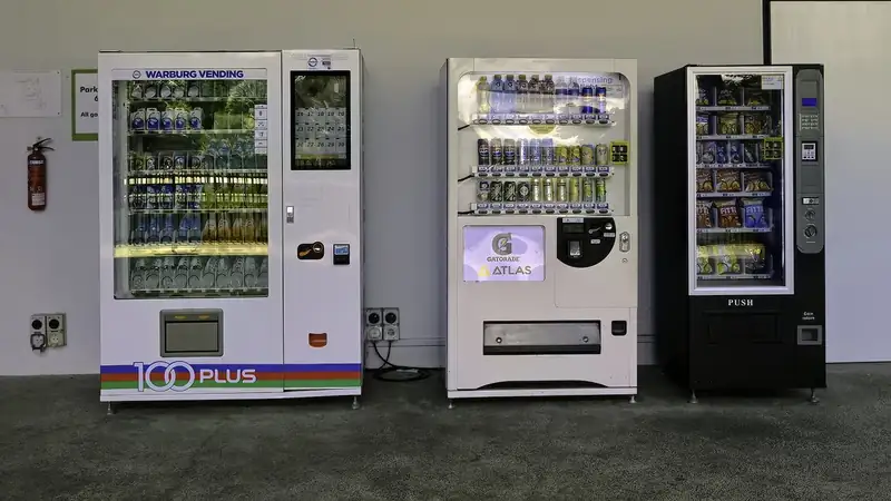 Three drink and snack vending machines standing side by side against a plain wall.