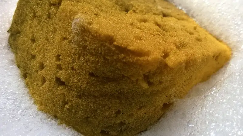 A soapy yellow car-wash sponge resting on a bed of white suds.